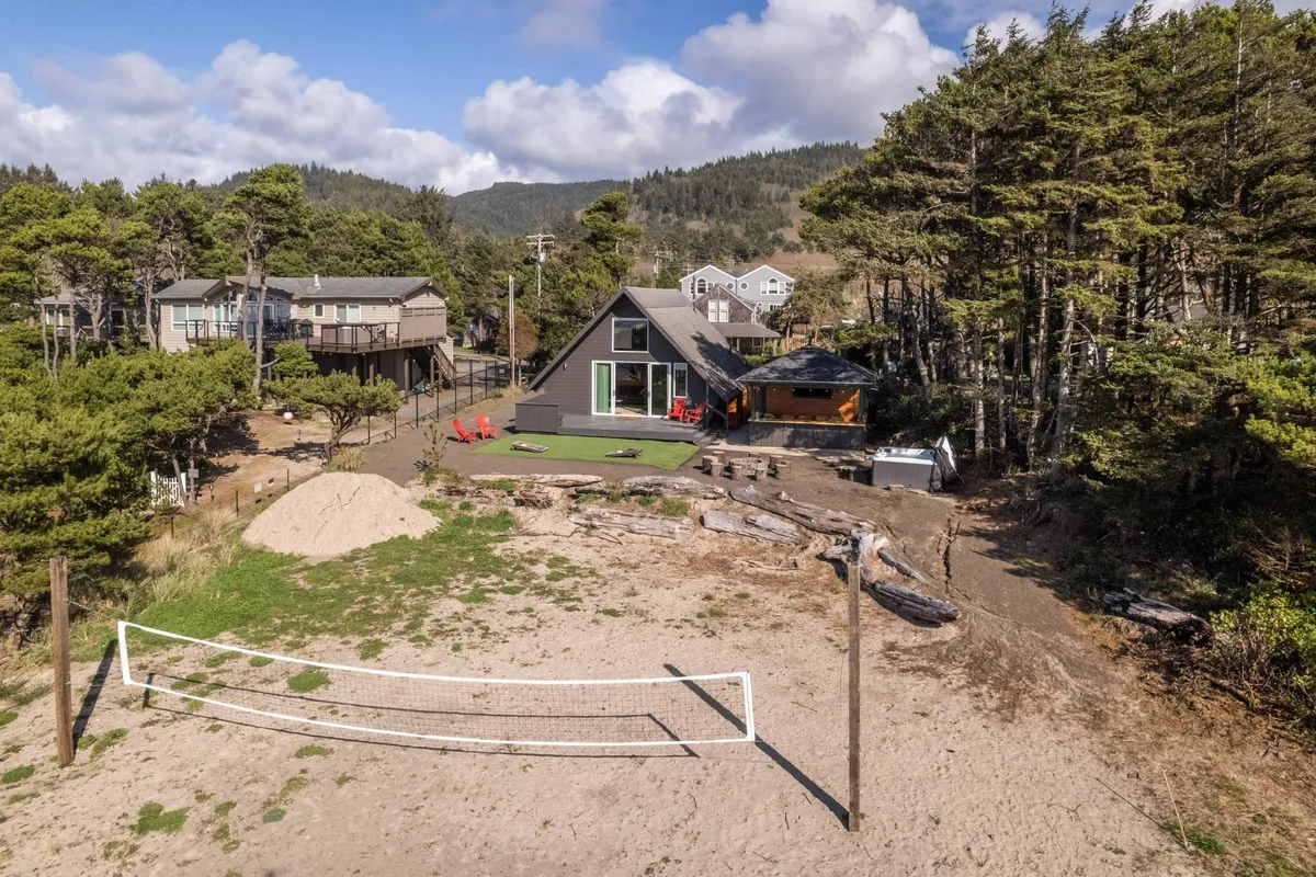 A modern house surrounded by trees with a visible volleyball net, ample seating, and open green spaces, suggesting room for lawn games, picnics, and relaxed outdoor gatherings.