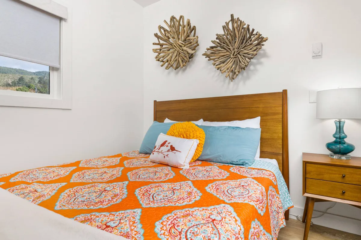 A cozy and inviting bedroom with a colorful quilt on a queen bed, decorative wall art, and a nightstand with a lamp. Warm natural light creates a restful atmosphere, perfect for relaxation and private moments.