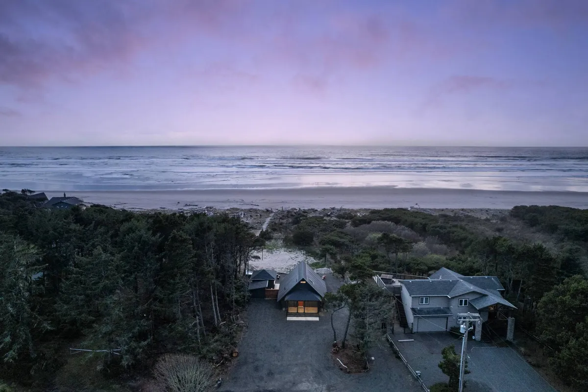 A sweeping view of the sandy beach meeting the Pacific Ocean, framed by houses and trees along the coastline. The calm waves and open sky evoke a sense of peace and invite beachcombing, evening strolls, and outdoor adventures.