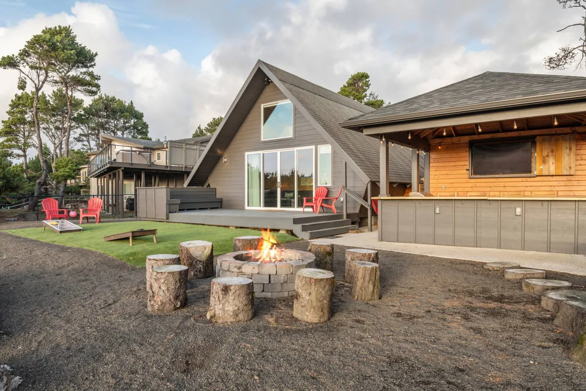 A cozy outdoor firepit area surrounded by red Adirondack chairs sits on a spacious wooden deck. Large windows reflect the surrounding trees and hint at the inviting interiors, while the setup encourages socializing and unwinding after a productive workday.