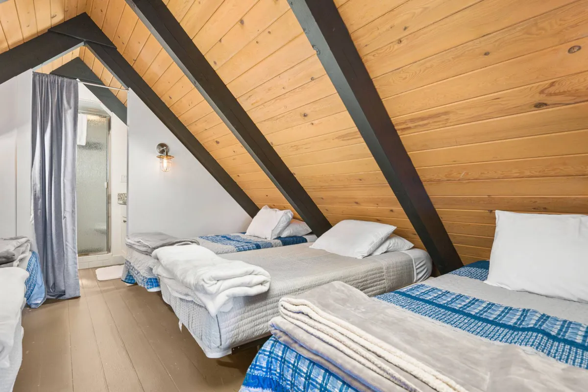 A cozy, lofted sleeping space inside the A-frame, with multiple beds and warm, communal decor. The layout encourages shared experiences, laughter, and late-night conversations among friends or family.